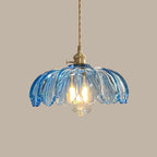 Blue glass Clérachic pendant with a petal-edged shade and a lit bulb, on a taupe backdrop.