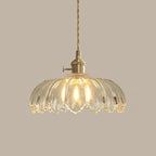 Clear glass Clérachic pendant with ribbed petals, lit warm, hanging from a twisted cord on a taupe backdrop.