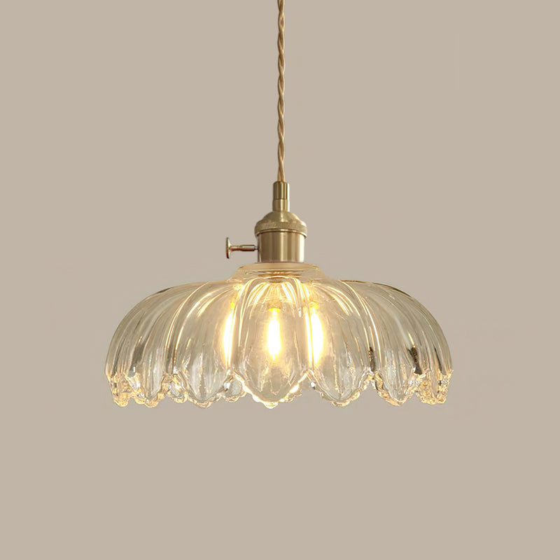 Clear glass Clérachic pendant with ribbed petals, lit warm, hanging from a twisted cord on a taupe backdrop.