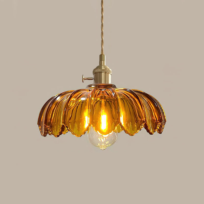 A lit amber glass Clérachic pendant with a rich, deep petal-edged shade, on a taupe backdrop.