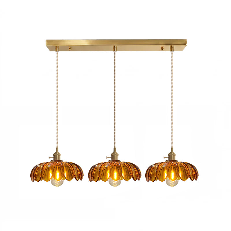 Row of three amber glass Clérachic pendants hanging from one long brass ceiling bar on a white backdrop.