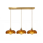 Row of three amber glass Clérachic pendants hanging from one long brass ceiling bar on a white backdrop.