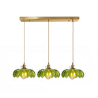 Row of three green glass Clérachic pendants hanging from one long brass ceiling bar on a white backdrop.