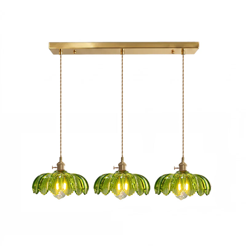 Row of three green glass Clérachic pendants hanging from one long brass ceiling bar on a white backdrop.