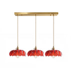 Row of three red glass Clérachic pendants hanging from one long brass ceiling bar on a white backdrop.