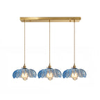 Row of three blue glass Clérachic pendants hanging from one long brass ceiling bar on a white backdrop.
