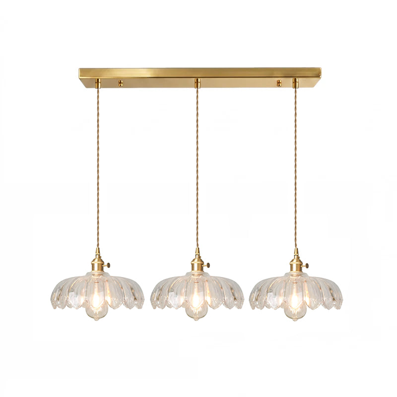 Row of three clear glass Clérachic pendants hanging from one long brass ceiling bar on a white backdrop.