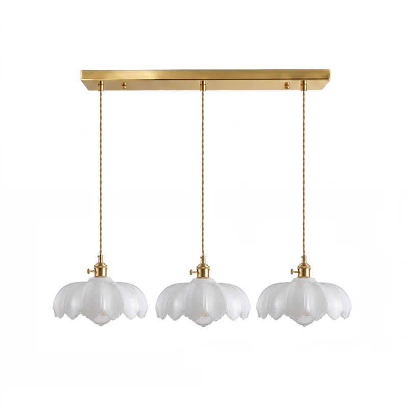 Row of three white glass Clérachic pendants hanging from one long brass ceiling bar on a white backdrop.
