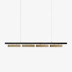 A Clérachic linear pendant with a slim black bar and four brass-toned diffusers, hung on two thin wires against a plain white backdrop.