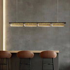Lit Clérachic linear pendant with four brass diffusers hung over a breakfast bar with tan leather stools and a grey concrete-effect wall.