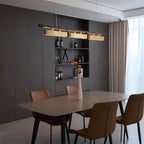 Three-head Clérachic pendant with brass diffusers above a dining table, seen at an angle beside a wine shelf and cream curtains.