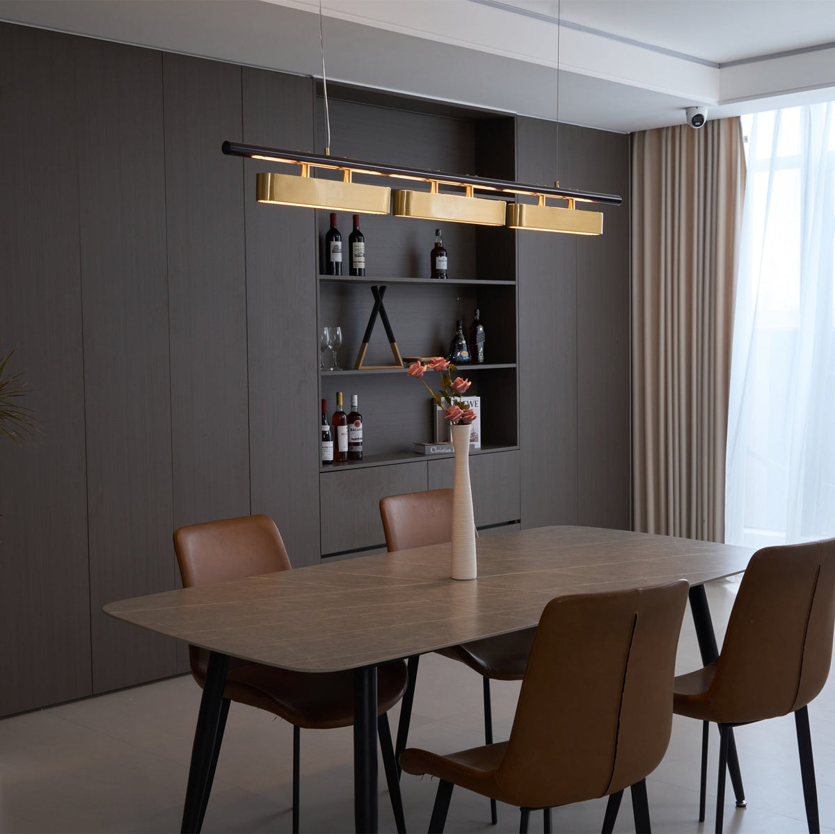 Three-head Clérachic pendant with brass diffusers above a dining table, seen at an angle beside a wine shelf and cream curtains.