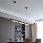 Angled view of a Clérachic brass pendant on two brass canopies, hung in a dining room with grey panelling and a white ceiling.