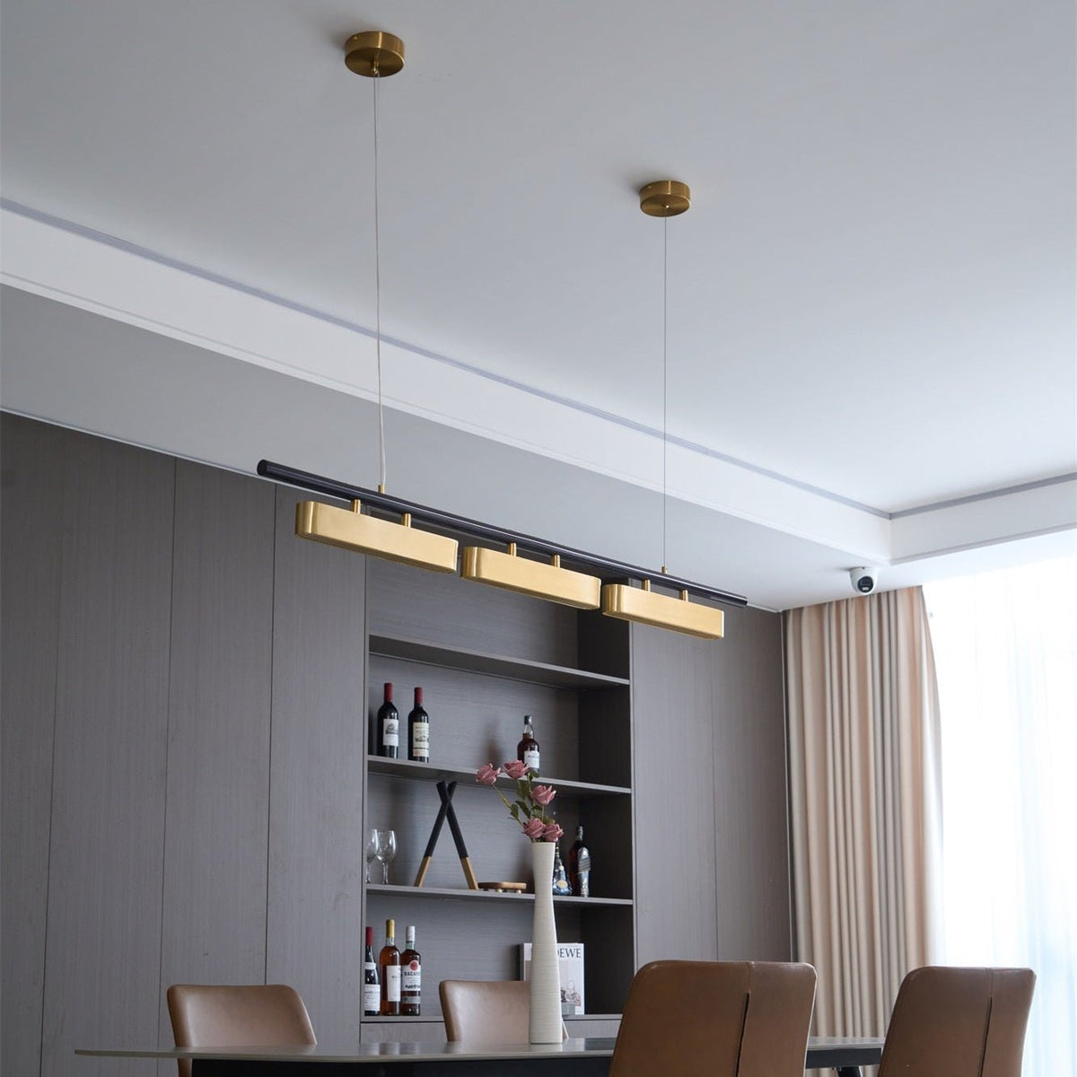Angled view of a Clérachic brass pendant on two brass canopies, hung in a dining room with grey panelling and a white ceiling.