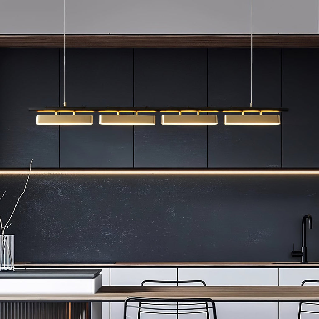 Four brass diffusers glow on a Clérachic linear pendant above a dark kitchen, with a black splashback and a pale worktop below.