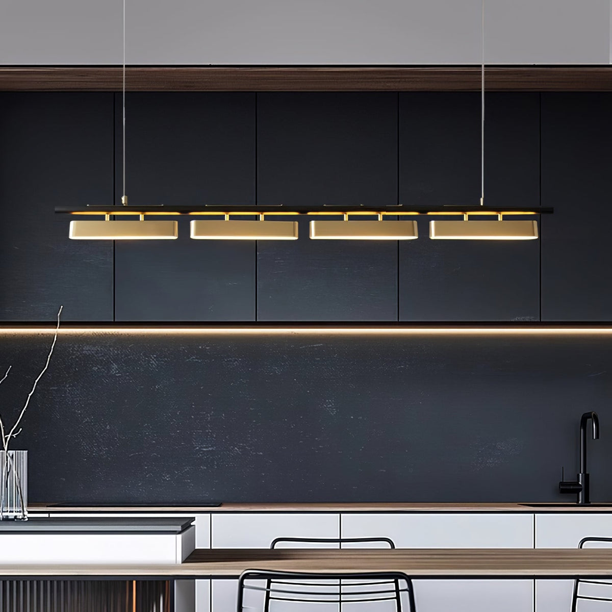 Four brass diffusers glow on a Clérachic linear pendant above a dark kitchen, with a black splashback and a pale worktop below.