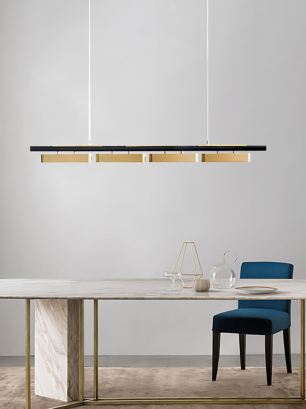 Clérachic linear pendant with four brass heads above a marble dining table, with a blue velvet chair and gold-legged base beside it.