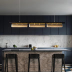 Three-head Clérachic brass pendant above a kitchen island with black stools, navy cabinets and a marble-effect splashback.