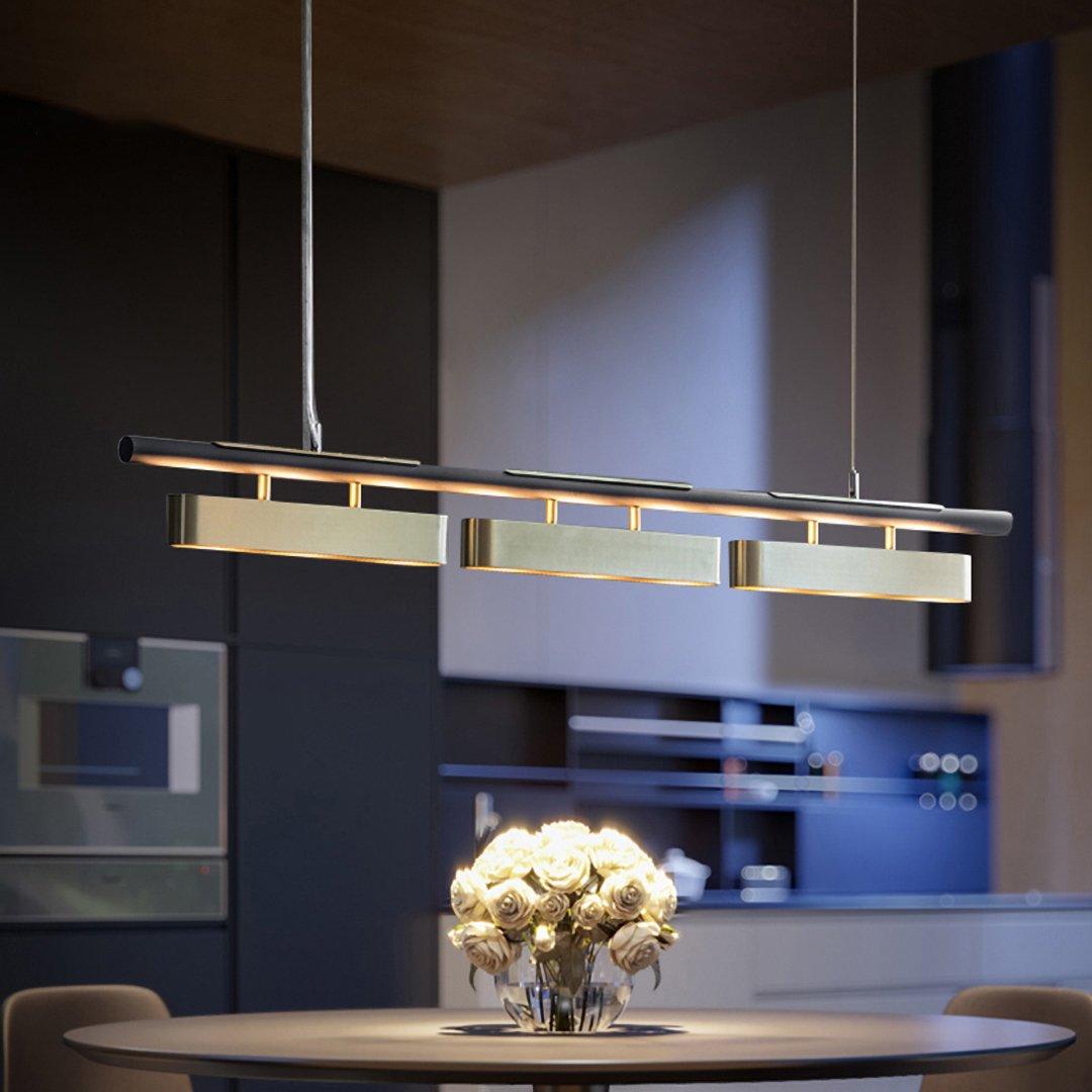 Clérachic linear pendant with three brass diffusers hung low over a dining table in a dark, moody kitchen with a round vase of white roses.