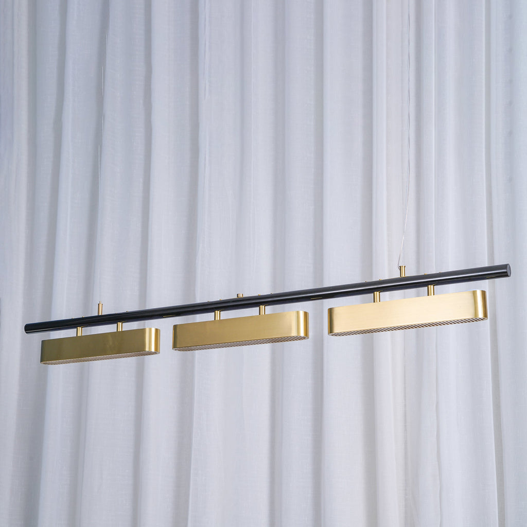 Clérachic linear pendant with three brass diffusers hung at a slant against sheer white curtains, the black bar catching the light.