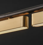 Close view of the brushed brass housing and slatted lit panels on this Clérachic linear pendant, against a near-black background.