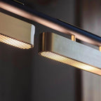 Close view of two lit slotted panels and a brushed brass side on this Clérachic linear pendant, against a dark blurred room.