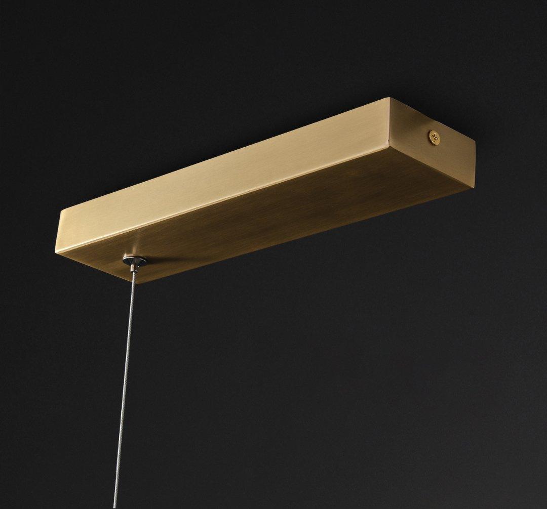 Close view of the brass rectangular canopy and thin suspension cable on this Clérachic linear pendant, against a black background.