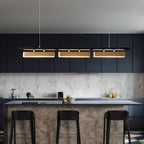 Lit three-head Clérachic pendant above a kitchen island with black stools, a marble-effect splashback and navy cabinets.
