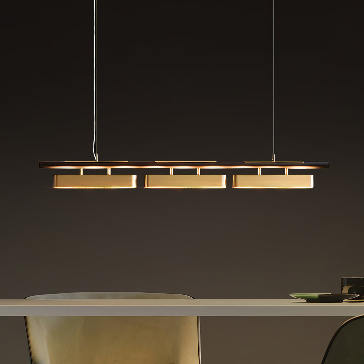 Clérachic linear pendant with three brass heads above a pale table, seen from the side against a dark grey wall.