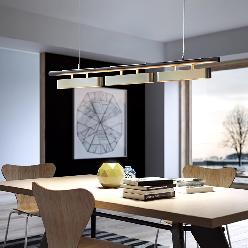 Clérachic three-head pendant above a wooden dining table with moulded chairs and a large window onto bare winter trees.