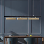 Three-head Clérachic brass pendant on a navy panelled wall, hung above a wooden table with dark green chairs.