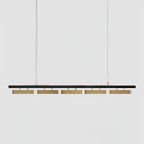 A five-head Clérachic linear pendant on a light grey backdrop, with a slim black bar and brass diffusers hung on two wires.