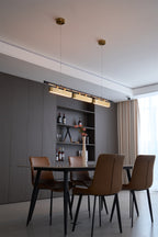 Distant view of a Clérachic pendant on two brass canopies, above a dining table with tan chairs and a wine shelf.