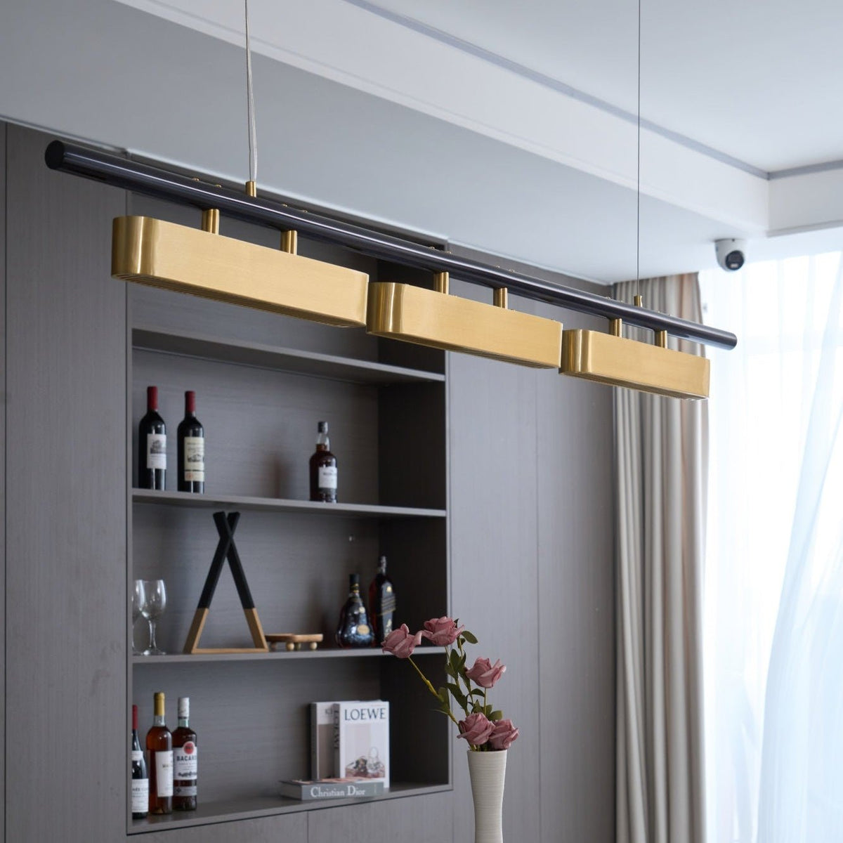 Close view of this Clérachic brass pendant above a wine shelf and cream curtains, its black bar angled across the frame.