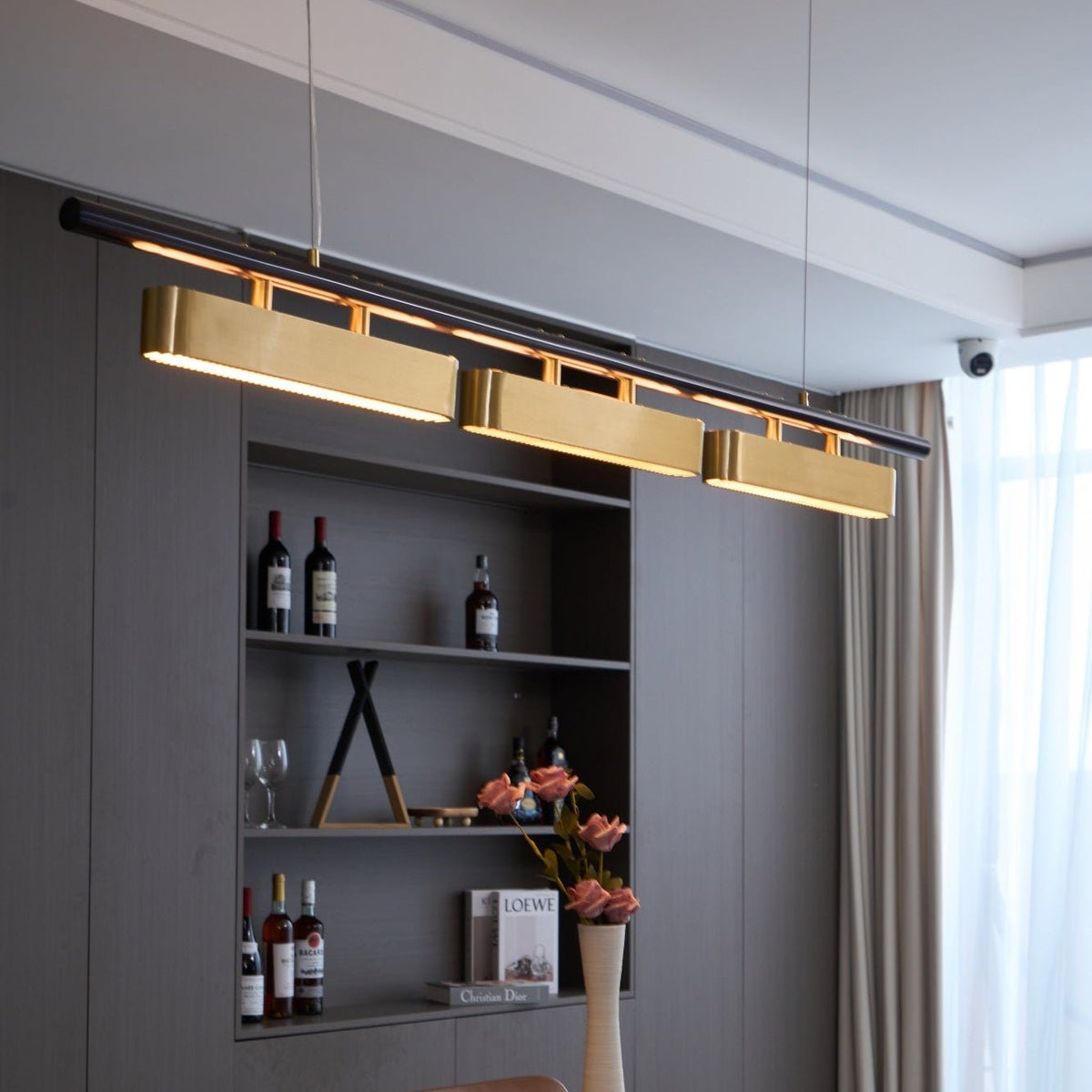 Close, low view of the lit Clérachic pendant, with warm light along the black bar above each brass diffuser.