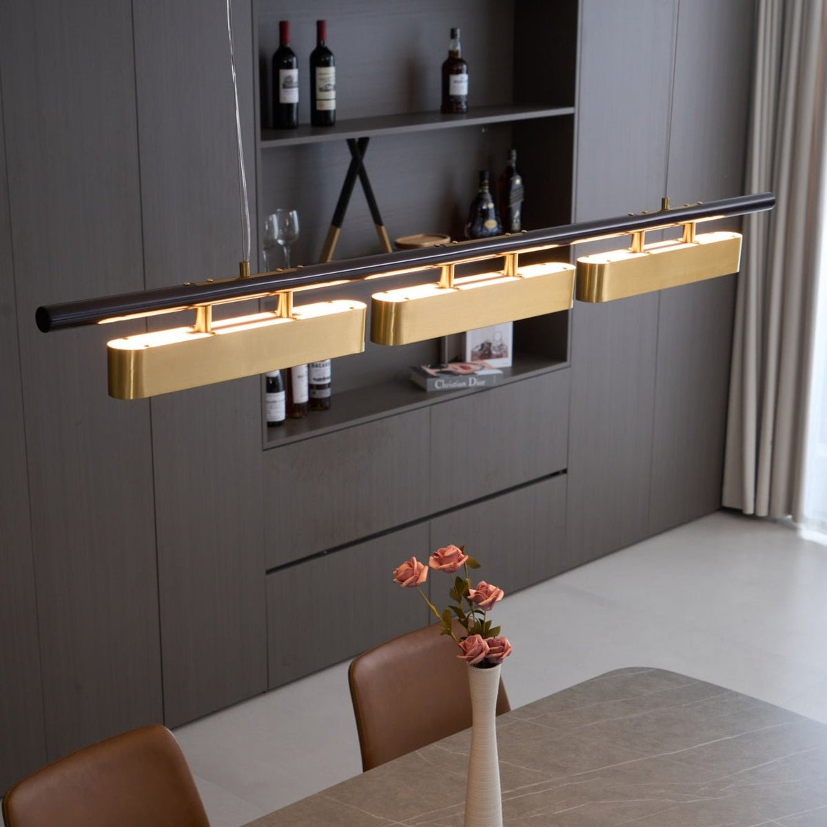 Close view from below of this Clérachic brass pendant, with a wine shelf, a vase of pink flowers and a table beneath.