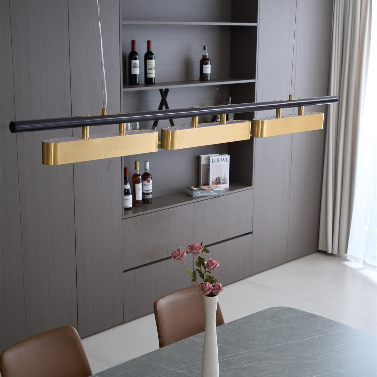 Close view of the Clérachic three-head pendant, with its brass diffusers aligned along a black bar above a shelf of bottles.