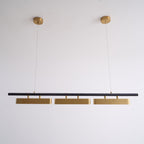 Unlit Clérachic three-head pendant on a white wall, hung from two round brass canopies on thin wires.