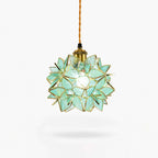 A Clérachic pendant light with a green glass petal shade, a brass socket and a braided cord, shown on a plain white backdrop.