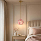 This Clérachic pendant with pink petals hangs by a ribbed cream headboard, over a bedside table with a gold-trimmed tray.