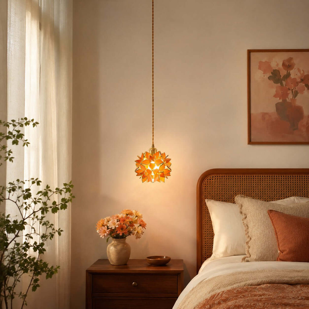 Orange glass petals light up this Clérachic pendant, hung beside a cane headboard and a wooden bedside table with orange flowers.