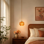 Orange glass petals light up this Clérachic pendant, hung beside a cane headboard and a wooden bedside table with orange flowers.