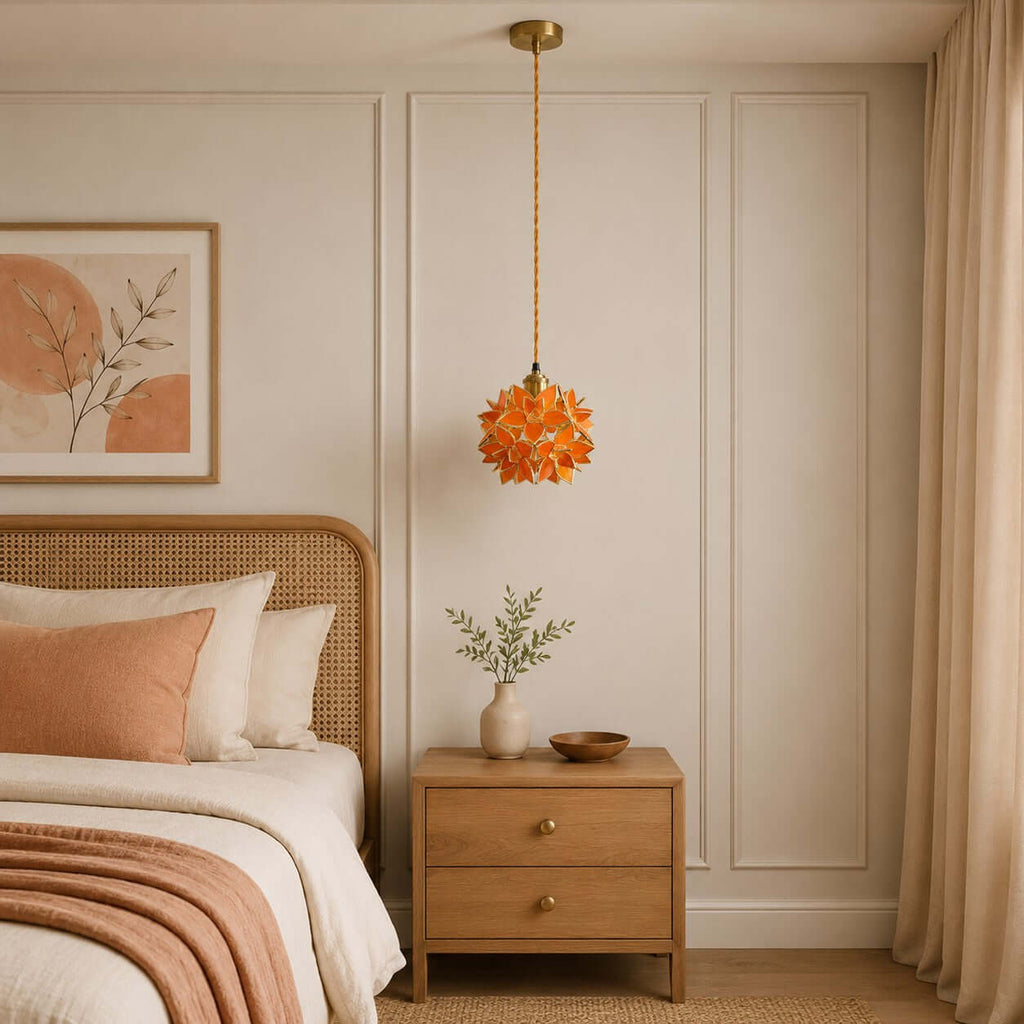 A small orange petal Clérachic pendant hangs on a brass fitting beside a cane bed, with a light oak bedside chest below.