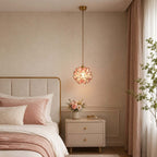 Pink Clérachic petal pendant lit beside a bed with a cream headboard, rose cushions and a pot of pink flowers on the nightstand.