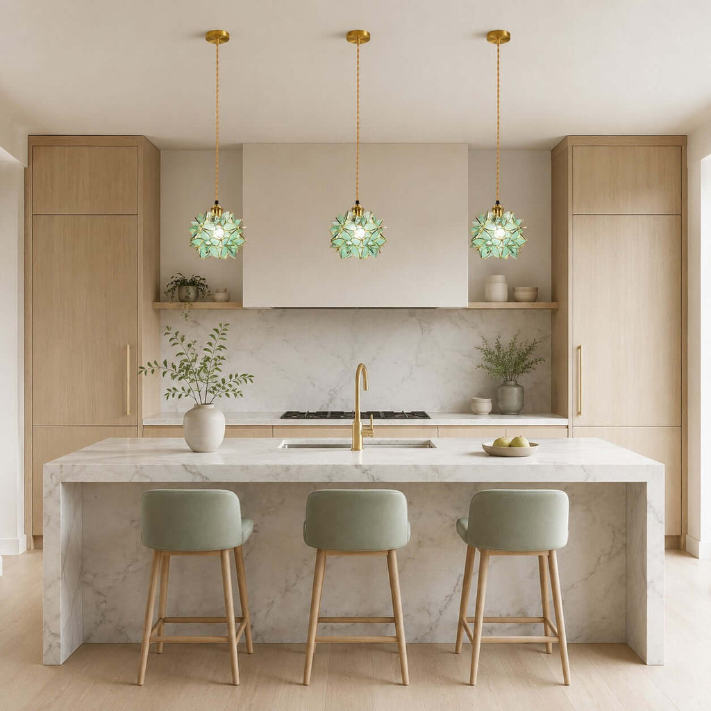 Three green petal Clérachic pendants hang in a row above a marble kitchen island with sage-green bar stools.