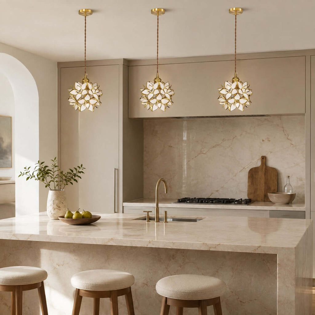 Three white glass petal Clérachic pendants hang in a line before a kitchen with a marble splashback and round stools.