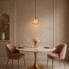 Pink petal Clérachic pendant glowing over a set round table with two rose velvet chairs, in a warm taupe niche room.