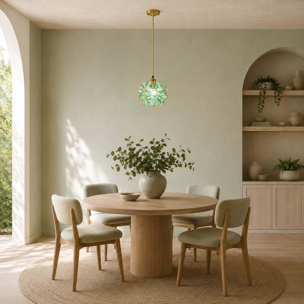 A green glass petal Clérachic pendant hangs over a round wooden table in a sage-green room with shelving in an arched alcove.