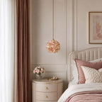 Clérachic pendant with soft pink petals hangs by a dusty-rose curtain, above a round bedside table and a bed with pink bedding.