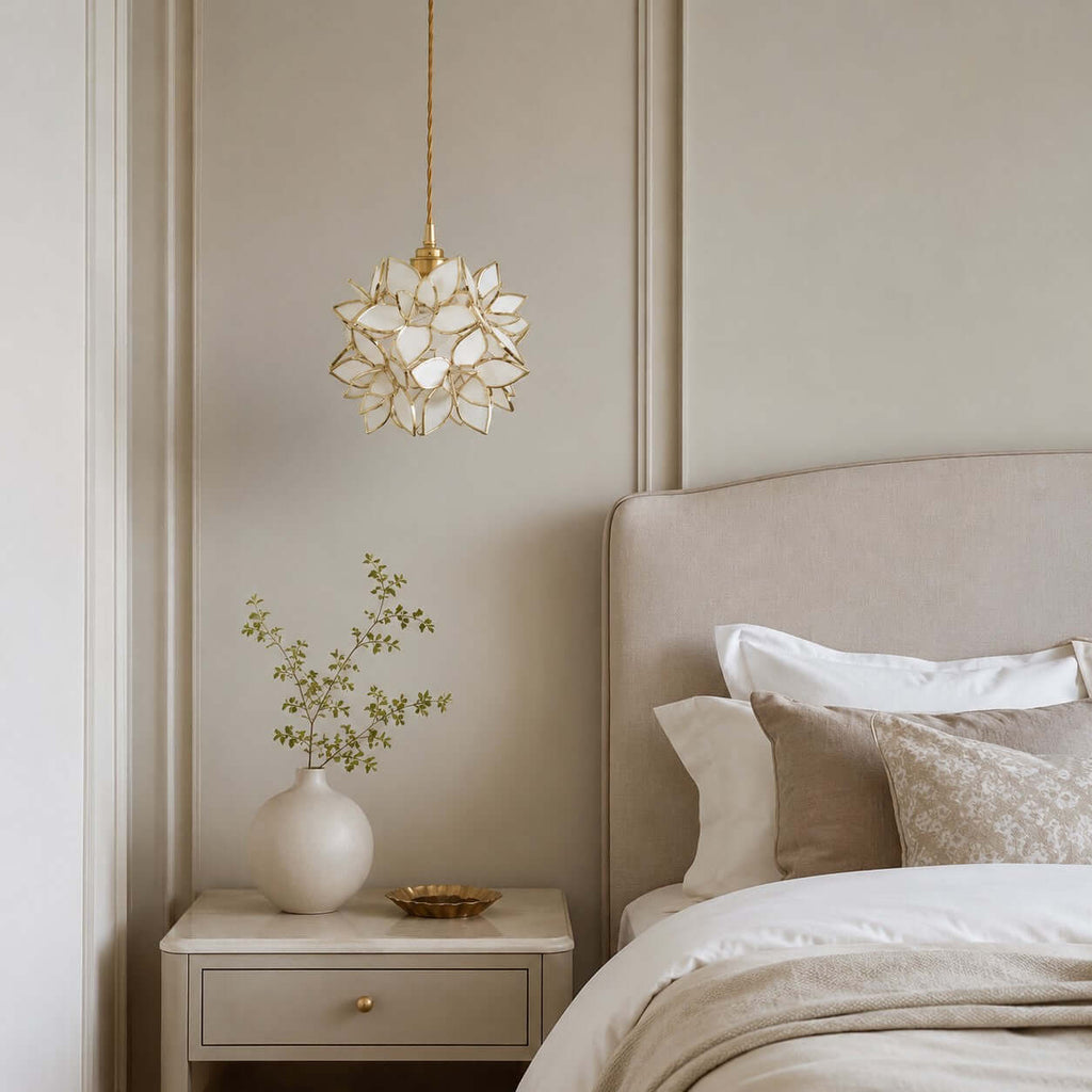 Small white petal Clérachic pendant hanging high above a cream headboard and a bedside table with a vase of green stems.